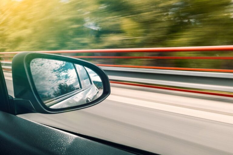 Zijspiegel van een rijdende auto op de snelweg, symbool voor je eerste autoverzekering en zelfstandig de weg op gaan