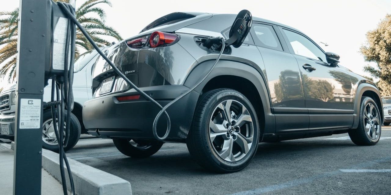 Grijze elektrische auto aan het laden op een zonnige parkeerplaats, voorbeeld van elektrisch rijden onderweg