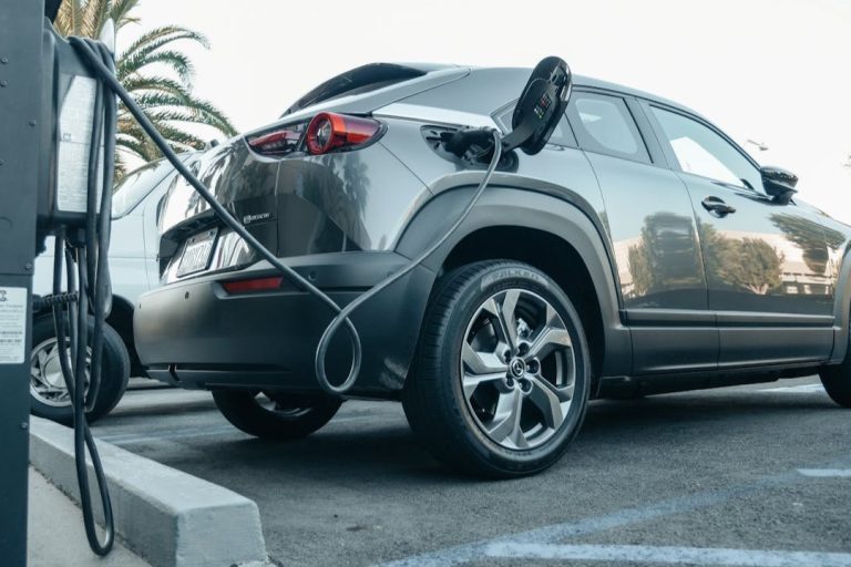 Elektrisch laden parkeerplaats Grijze elektrische auto aan het laden op een zonnige parkeerplaats, voorbeeld van elektrisch rijden onderweg