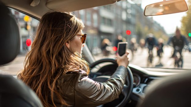 Jonge bestuurder gebruikt een smartphone in druk verkeer, een veelvoorkomende afleiding voor jonge bestuurders.